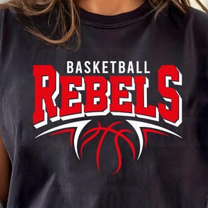 Puede incluir: Camiseta negra con las palabras "BASKETBALL REBELS" en letras rojas y blancas, con un gráfico de baloncesto rojo. La camiseta tiene las mangas dobladas.