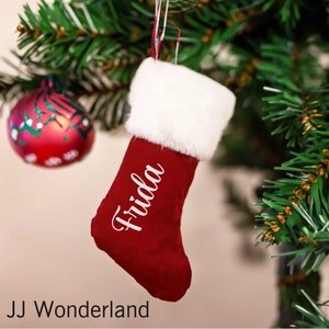 May include: Red felt Christmas stocking with a white faux fur cuff and the name "Frida" embroidered in white on the front.