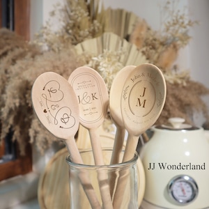 Könnte beinhalten: Drei Holzlöffel mit personalisierten Gravuren. Die Löffel befinden sich in einem Glasgefäß. Die Gravuren beinhalten "J&K" mit dem Datum "18:00 | 2021", "John & Michelle" mit den Initialen "J&M" und dem Datum "Samstag, 8. August 2020", sowie "Lisa & David" mit einem Herz- und Pfeilmotiv.