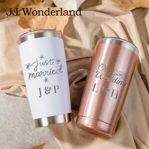 Könnte beinhalten: Zwei Edelstahlbecher mit personalisierten Gravuren. Der weiße Becher sagt "Just married" mit den Initialen "J&P". Der roségoldene Becher sagt "Our Wedding" mit den Initialen "L&H".
