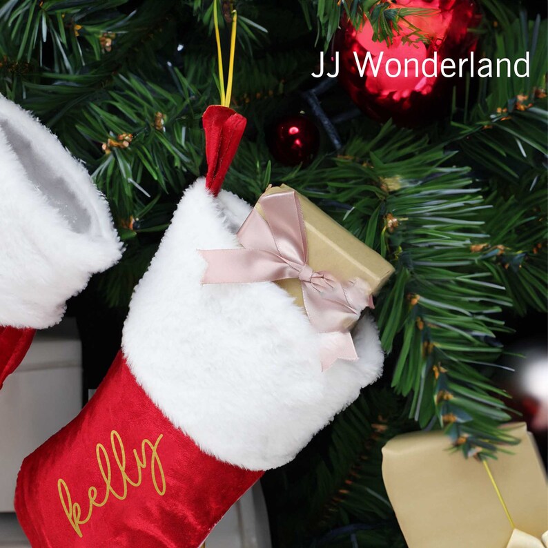 May include: Red velvet stocking with white faux fur cuff, personalized with the name "kelly" in gold lettering. A small gift box with a pink ribbon is inside the stocking.