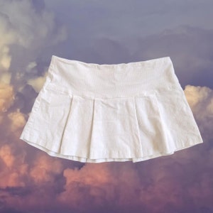 May include: A white pleated skirt made of corduroy. The skirt is mini length and has a simple design.