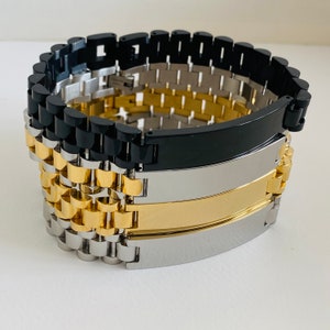 May include: A set of three metal bracelets with engraved plates. The bracelets are black, silver, and gold.