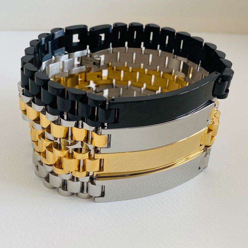 May include: A set of three metal bracelets with engraved plates. The bracelets are black, silver, and gold.