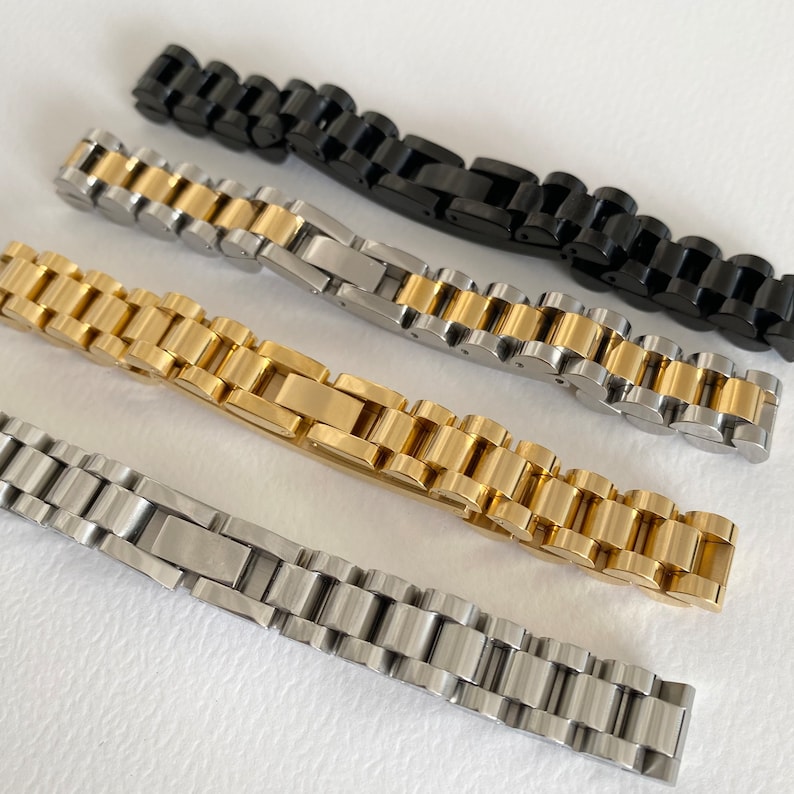 May include: Four watch bands in different finishes: black, gold, silver, and two-tone gold and silver. The bands are made of metal and have a classic link design.