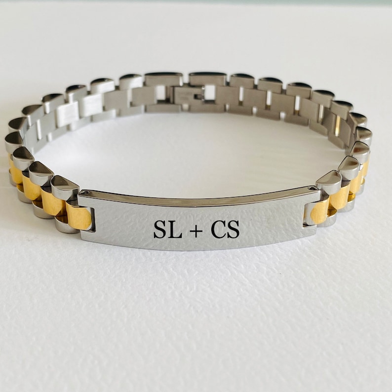 May include: A silver and gold bracelet with a rectangular tag engraved with the initials "SL + CS".