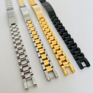 May include: Four metal watch bands in silver, gold, and black. The bands are made of linked metal pieces.