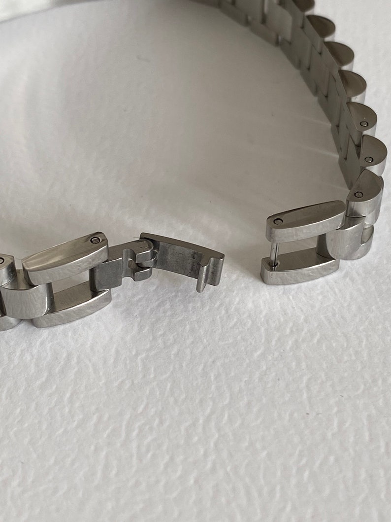 May include: A silver watch band with a clasp that is open. The band is made of metal links.