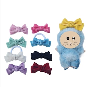 May include: A collection of colorful velvet hair bows in pink, teal, white, purple, blue, black, and red. A plush blue cat-shaped hair accessory with a yellow bow is also included. These hair accessories are perfect for adding a touch of flair to any hairstyle.