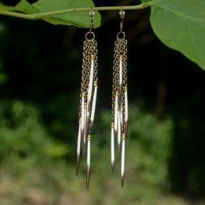 May include: A pair of long, dangling earrings with a gold chain and white feather-like accents.