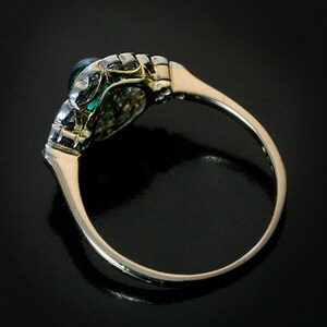 May include: An antique ring with a gold band and a dark green gemstone. The setting features intricate filigree and small accent stones. The ring is shown against a dark background, highlighting its details.