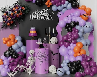 May include: A Halloween party decoration with purple, orange, and black balloons, a skeleton, a spider web, and a cake. The backdrop is a black chalkboard with the words "Happy Halloween" written in white chalk.