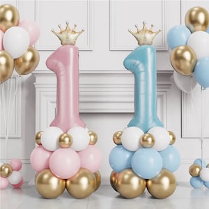 May include: Two large number one balloons, one pink and one blue, with gold crowns on top. Each balloon is surrounded by smaller balloons in gold, white, and pink or blue.