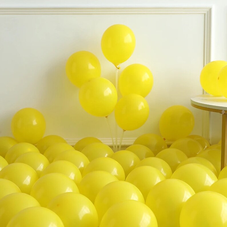 May include: A large group of yellow balloons, some tied together in a cluster, with others scattered on the floor.