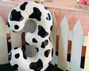 May include: A large, white and black cow print number three balloon. The balloon is inflated and ready to be used for a party or celebration.