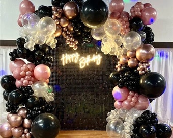 May include: A black and rose gold balloon arch with the words "Happy Birthday" in neon lights. The balloons are arranged in a cascading pattern and are tied to a black sequin backdrop.