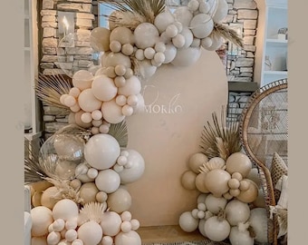 May include: A beige and white balloon arch with dried floral accents and a light pink backdrop. The word "Morro" is written on the backdrop. The arch is decorated with various sizes of balloons, creating a festive and elegant display.