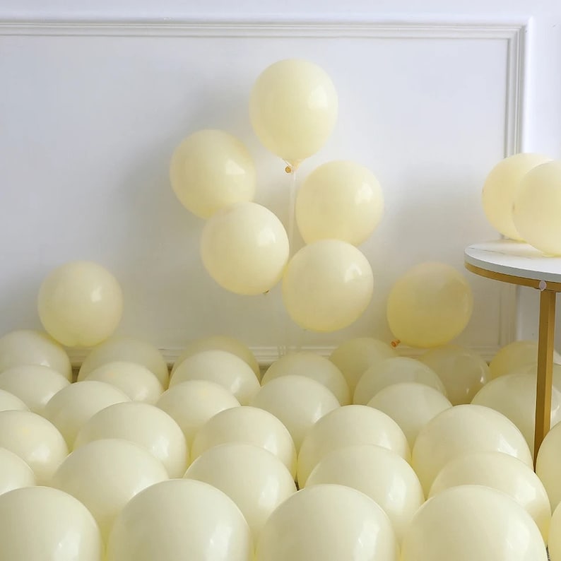 May include: A large group of cream-colored balloons, with a smaller group of balloons tied together in a cluster on a white wall.