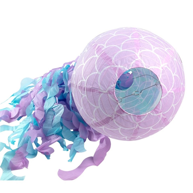 Op de afbeelding: Een paarse en blauwe papieren lantaarn met een zeemeermin-schubbenpatroon. De lantaarn heeft een wit draadframe en is versierd met een lange, stromende streamer van paars en blauw tissuepapier.