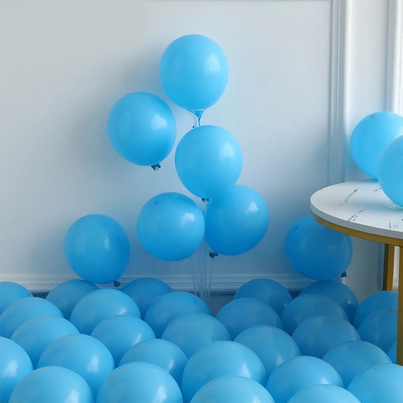 Peut inclure: Un groupe de ballons bleu clair, certains li&eacute;s ensemble et d'autres &eacute;parpill&eacute;s sur le sol. Les ballons sont dispos&eacute;s en grappe, avec certains ballons flottant dans l'air.