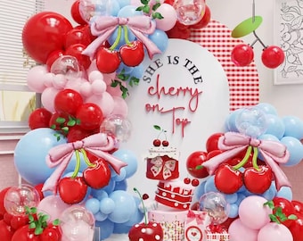 Pode incluir: Uma cena festiva com balões vermelhos, rosa e azuis, decorações de cerejas e um bolo. As palavras "She is the cherry on top" são exibidas em um arco branco. Laços decorativos e balões transparentes contribuem para a atmosfera festiva.