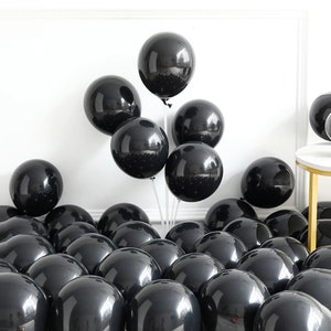 K&ouml;nnte beinhalten: Eine gro&szlig;e Gruppe schwarzer Ballons, einige zusammengebunden und andere auf dem Boden verstreut. Die Ballons sind gl&auml;nzend und reflektieren das Licht.