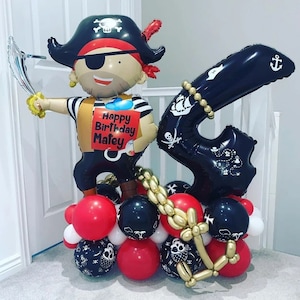 May include: A black and gold balloon arch with a pirate character balloon holding a sign that says "Happy Birthday Matey".