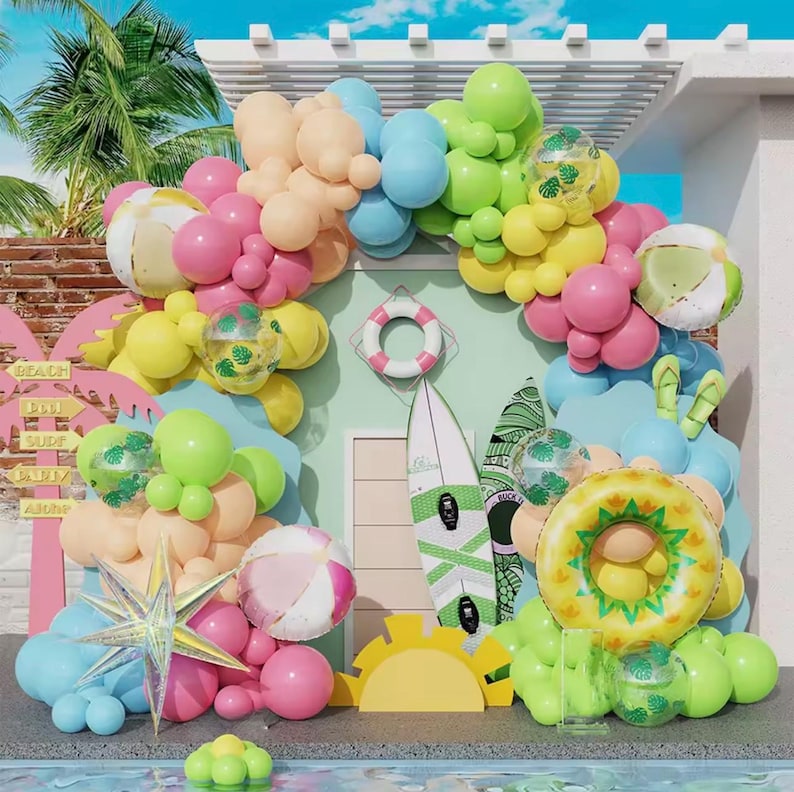 May include: A colourful beach-themed display with balloons in pink, yellow, blue, and green. The arrangement includes beach balls, a life preserver, surfboards, and a pineapple-shaped float, creating a festive summer scene.