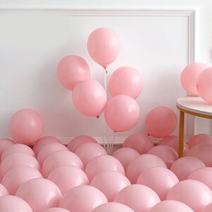 Peut inclure: Un grand groupe de ballons roses, certains attach&eacute;s et flottants, d'autres &eacute;parpill&eacute;s sur le sol.