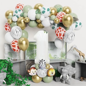 May include: A white number one balloon with a jungle animal theme. The balloon is surrounded by green, gold, and white balloons. There are also balloons with a zebra and giraffe print. The number one balloon has a zebra, monkey, and lion attached to it.