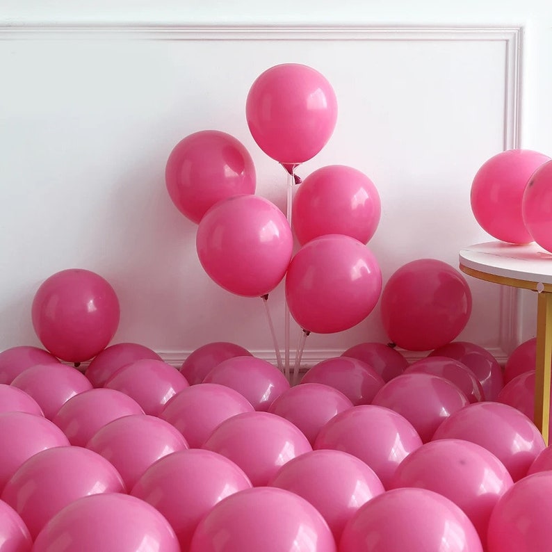 Peut inclure: Un grand groupe de ballons roses, avec quelques ballons attach&eacute;s ensemble avec de la ficelle et tenus par un support transparent. Les ballons sont dispos&eacute;s en demi-cercle sur une surface blanche.