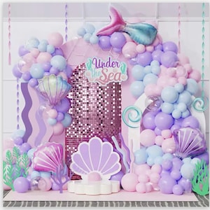 May include: A pink and purple balloon arch with a mermaid tail and "Under the Sea" banner. The arch is decorated with iridescent sequins and seashell decorations.