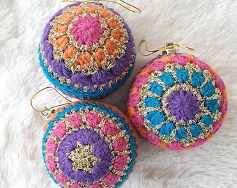 May include: Three crocheted Christmas ornaments in shades of purple, pink, orange, and teal with gold accents. Each ornament features a different geometric pattern.