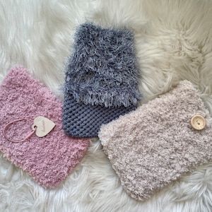 Könnte beinhalten: Drei flauschige Stoffbeutel in Rosa, Grau und Beige. Der rosa Beutel hat ein herzförmiges Etikett mit dem Wort "Handmade" darauf. Der graue Beutel hat einen Knopf. Der beige Beutel hat einen Knopf.