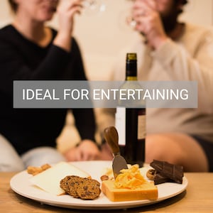 Puede incluir: Un plato blanco con queso, galletas y chocolate, junto a una botella de vino y un cuchillo para queso. El texto "IDEAL FOR ENTERTAINING" est&aacute; en la imagen.