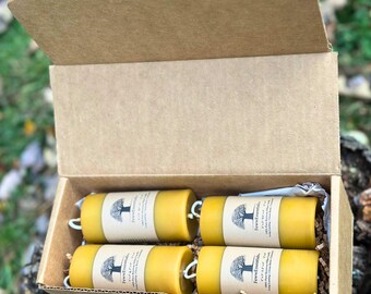 May include: A cardboard box containing four yellow beeswax candles. Each candle has a white wick and a label with a tree logo and the text "Few Essentials". The box is open, revealing the candles nestled inside.