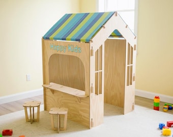 Può includere: Una casetta di legno con un tetto a strisce blu e verdi e le parole "Happy Kids" in azzurro. La casetta ha un bancone e due sgabelli piccoli. La casetta è su un tappeto bianco.