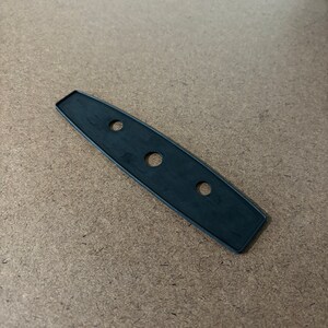 May include: A black, elongated rubber piece with three evenly spaced circular holes. The piece has a slightly curved shape and a matte finish. The edges are smooth and rounded.
