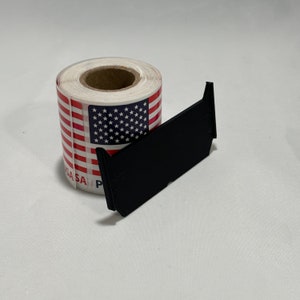 May include: A roll of stickers featuring the American flag design with red and white stripes and a blue square with white stars. A black, angled object rests beside the roll of stickers.