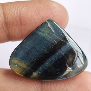 May include: A blue and gold tiger's eye gemstone cabochon with a teardrop shape. The stone has a reflective surface and a striated pattern.