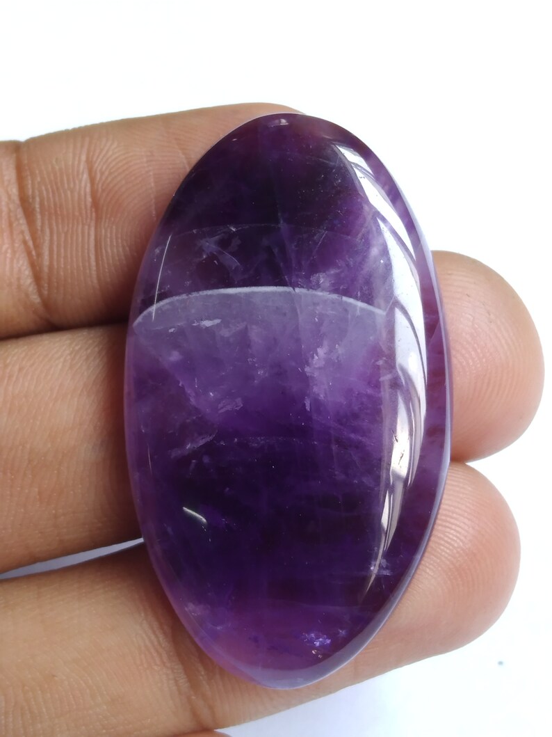 Puede incluir: Una gran piedra preciosa de amatista de forma ovalada, de color morado oscuro y superficie lisa y pulida.
