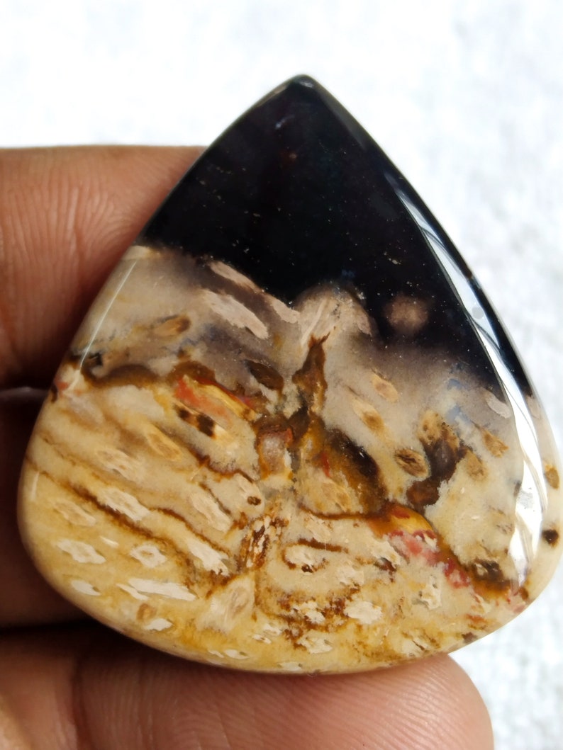 Pu&ograve; includere: Un cabochon di agata a forma di lacrima con un motivo nero, bianco, marrone e arancione. La pietra &egrave; lucidata e ha una superficie liscia.