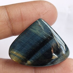 May include: A blue and gold tiger's eye gemstone cabochon in a teardrop shape.