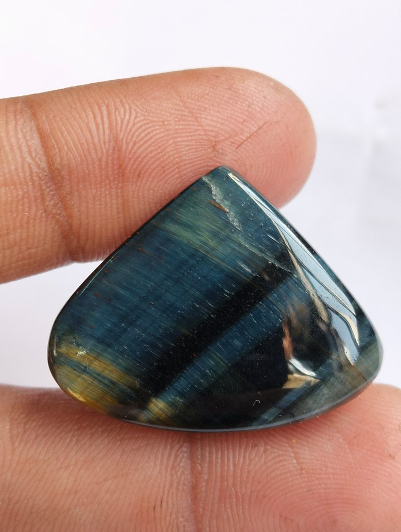 May include: A blue and gold tiger's eye gemstone cabochon in a teardrop shape.