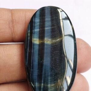May include: A blue and gold oval-shaped gemstone with a tiger's eye pattern. The gemstone is smooth and polished.