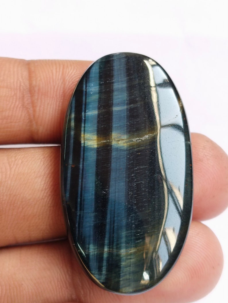 May include: A blue and gold oval-shaped gemstone with a tiger's eye pattern. The gemstone is smooth and polished.