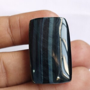 May include: A dark blue and black tiger's eye gemstone cabochon with a rectangular shape.