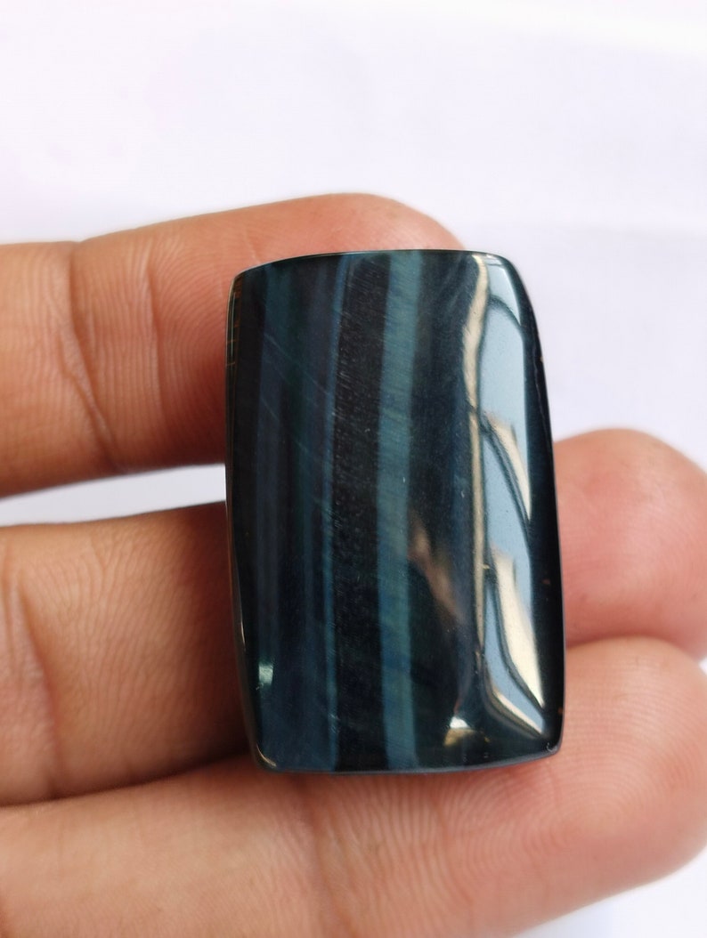 May include: A dark blue and black tiger's eye gemstone cabochon with a rectangular shape.