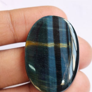 May include: A blue and gold oval-shaped gemstone with a tiger's eye pattern. The gemstone has a smooth, polished surface.