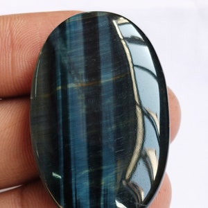 May include: A blue and gold oval-shaped gemstone with a tiger's eye pattern. The gemstone is smooth and polished.